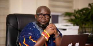 The Relentless Crusader: Ken Ashigbey and the Gospel According to the River Gods Ken Ashigbey, convener of the Media Coalition Against Galamsey, seated confidently at his office desk wearing traditional Ghanaian attire and bracelets, symbolizing his relentless advocacy against illegal mining in Ghana.