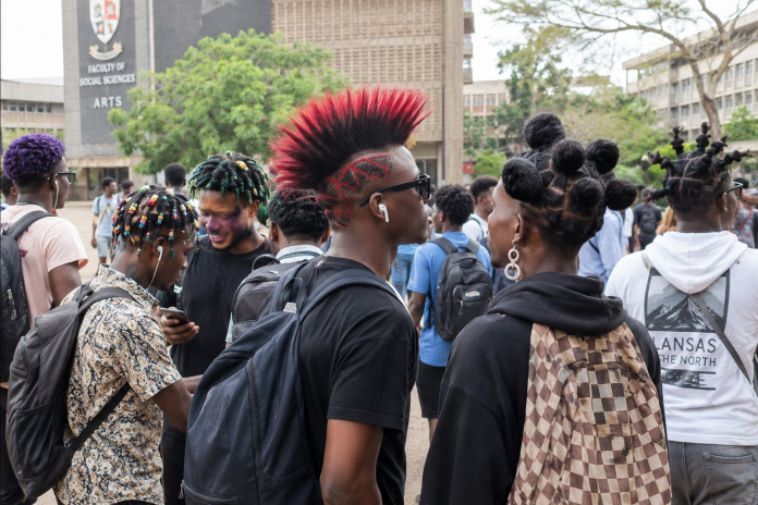 University Hairstyles Debate showing students with colourful hairstyles and earrings on a Ghanaian university campus.