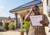 THE ONLY THING THAT FLOWS REGULARLY IS THE BILL ECG estimated billing in Ghana illustrated by a homeowner holding a high electricity bill beside rooftop solar panels